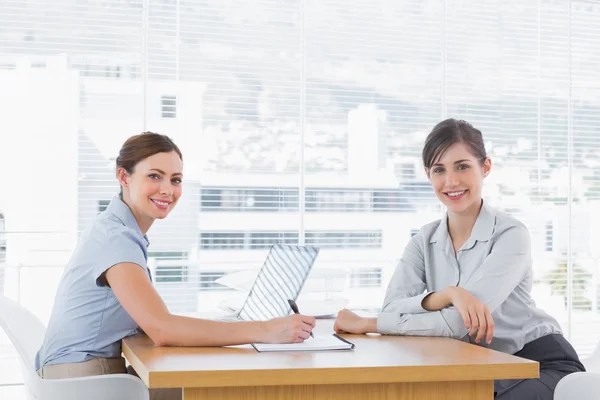 Empresárias tendo uma reunião na mesa e sorrindo para a câmera — Fotografia de Stock