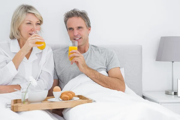 Pareja bebiendo jugo de naranja desayunando en la cama —  Fotos de Stock