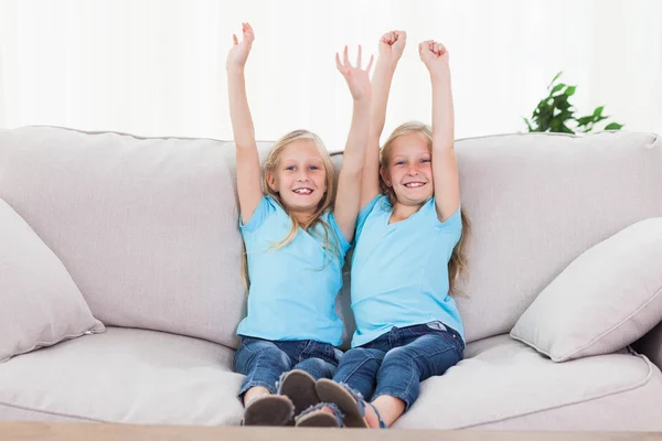 Twins raising their arms sitting on a couch — Stock Photo, Image