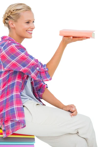 Beautiful woman showing a book and sitting on a stack of books — Stock Photo, Image