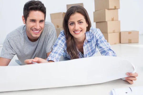 Portrait of a couple lying on the floor and holding a house plan — Stockfoto