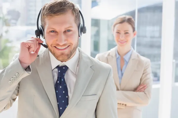 Handsome call centre agent with colleague behind him — Stock Photo, Image