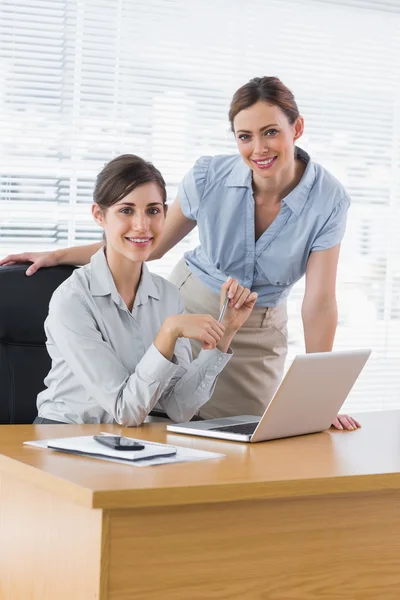 Happy businesswomen at desk smiling at camera — Stock Photo, Image