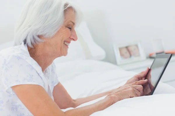 Frau benutzt Tablet, während sie im Bett liegt — Stockfoto