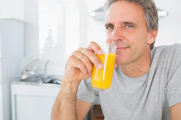 Ευτυχισμένος άνθρωπος πίνοντας χυμό πορτοκαλιού στην κουζίνα — Φωτογραφία Αρχείου
