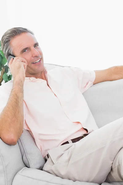Человек на диване делает телефонный звонок, улыбаясь в камеру — стоковое фото