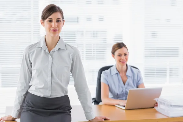 Businesswomen smiling at camera with one sitting and one standin — Stock Photo, Image
