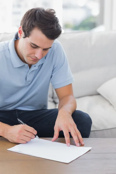 Man writing on a paper while he is sat on a couch Stock Image