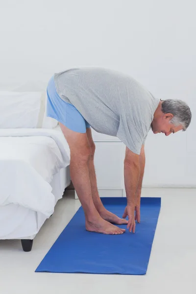 Uomo maturo che si estende su un tappeto aerobico — Foto Stock