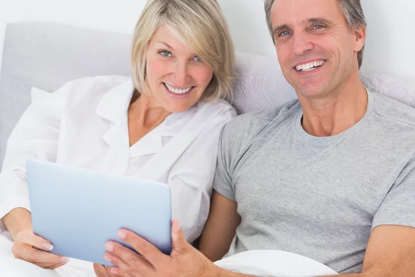 Couple using tablet pc in bed smiling at camera — Stock Photo, Image