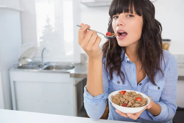 Cheerful brunette eating bowl of cereal and fruit — Stock Photo, Image