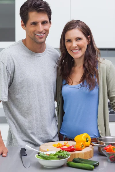 Alegre pareja sonriendo a la cámara y preparando verduras —  Fotos de Stock