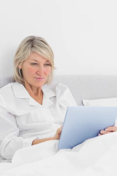 Mujer alegre sentada en la cama usando tableta pc — Foto de Stock