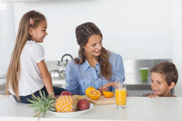 Mujer atractiva cortando una naranja para sus hijos —  Fotos de Stock