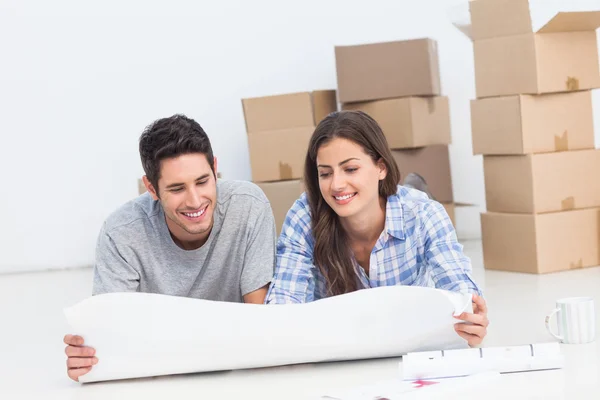 Couple lying on the floor and looking at house plans — Stock Photo, Image