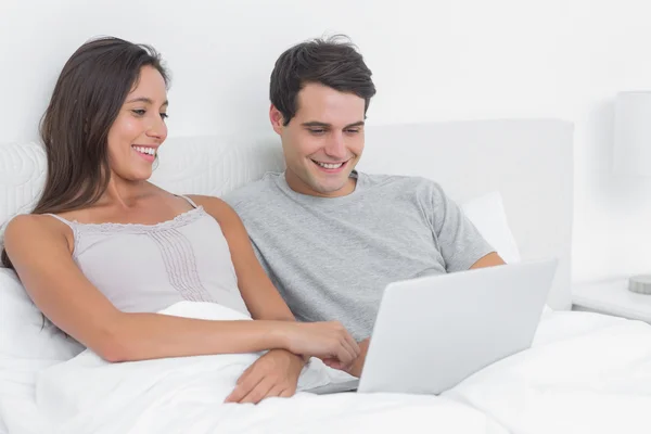 Casal usando um laptop juntos deitado na cama — Fotografia de Stock