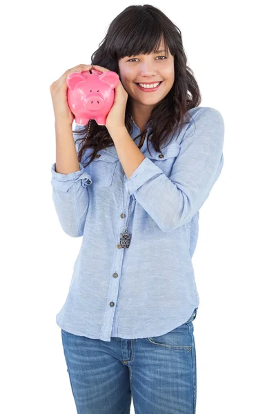 Smiling young woman shaking her piggy bank — Stock Photo, Image