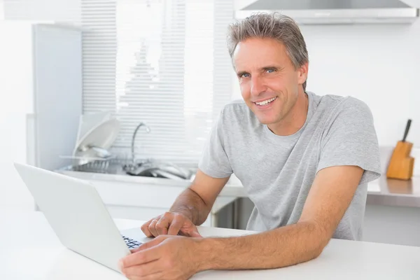 Homem alegre usando laptop na cozinha — Fotografia de Stock