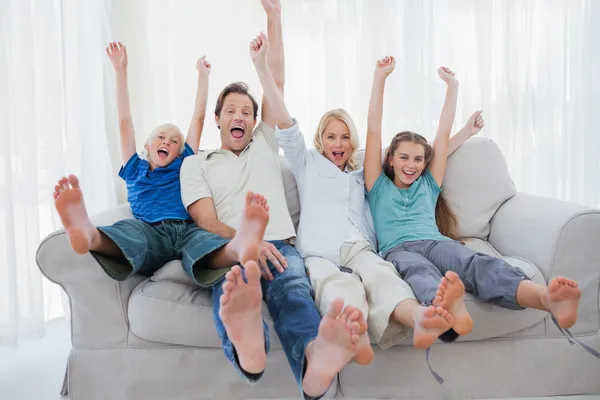 Family sitting on a couch and raising arms — Stockfoto