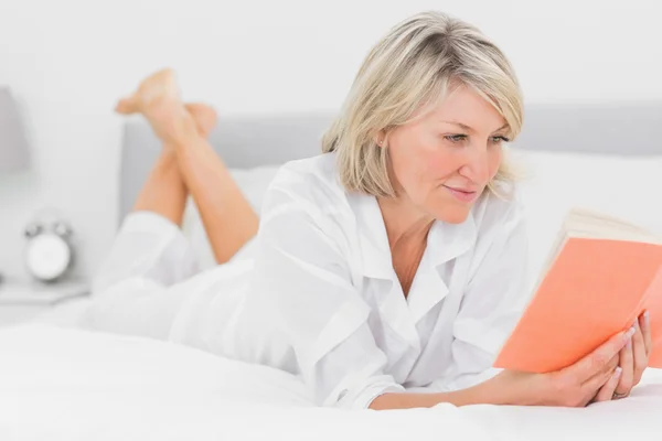 Cheerful woman reading a book lying on bed — Stock Photo, Image