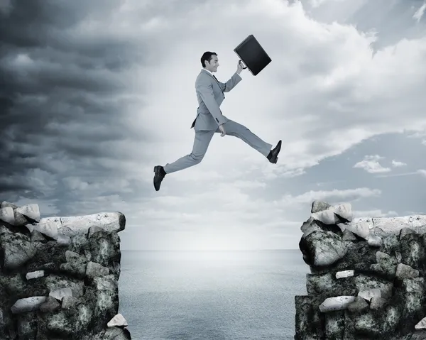 Businessman jumping a gap between cliffs — Stock Photo, Image