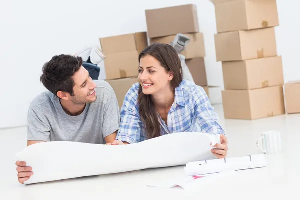 Couple lying on the floor and holding house plans — Stock Photo, Image