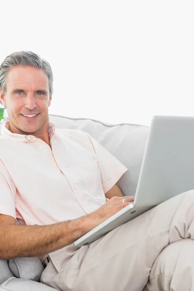 Sorrindo homem em seu sofá usando laptop olhando para a câmera — Fotografia de Stock