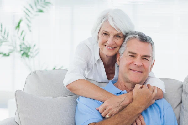 Woman embracing husband sitting on the couch — Stock Photo, Image