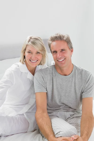 Sonriente pareja sentada en la cama — Foto de Stock