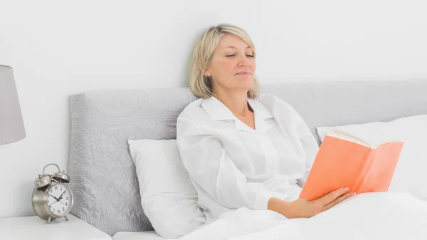Mujer rubia sentada en la cama leyendo — Foto de Stock