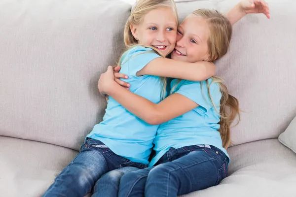 Young twins embracing each other sitting on a couch — Stock Photo, Image