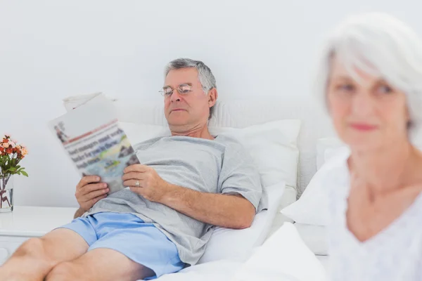 Reifer Mann liest Zeitung im Bett — Stockfoto