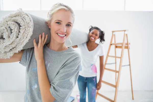 Glückliche Mitbewohner tragen zusammengerollten Teppich im neuen Zuhause — Stockfoto