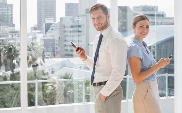 Glückliches Geschäftsteam, das Rücken an Rücken steht und SMS schreibt — Stockfoto