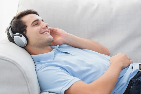 Hombre alegre disfrutando de la música tumbado en un sofá —  Fotos de Stock