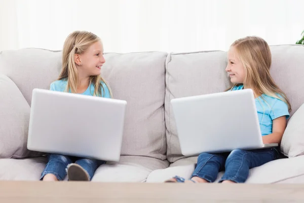 Cute twins using laptops sitting on a couch — Stock Photo, Image