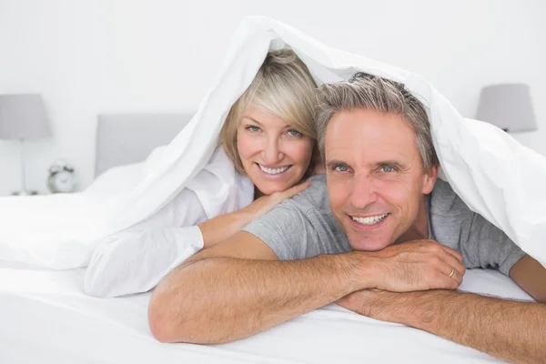 Felice coppia sorridente sotto le coperte alla fotocamera — Foto Stock