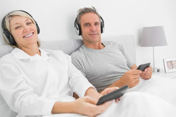 Sonriendo pareja a la música en sus teléfonos inteligentes — Foto de Stock