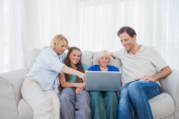 Family sitting on a couch while using a laptop — Stock fotografie