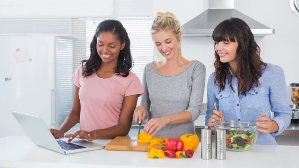 Happy friends making salad and using laptop for recipe — Stock Photo, Image