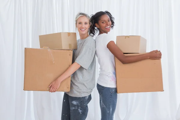 Happy friends standing back to back holding moving boxes — Stock Photo, Image