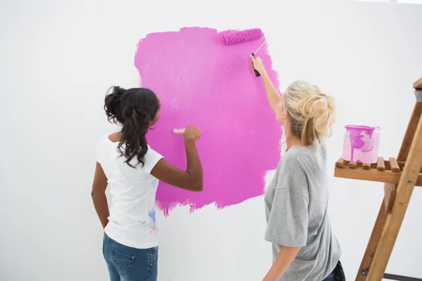 Felices compañeros de casa jóvenes pintando la pared rosa —  Fotos de Stock