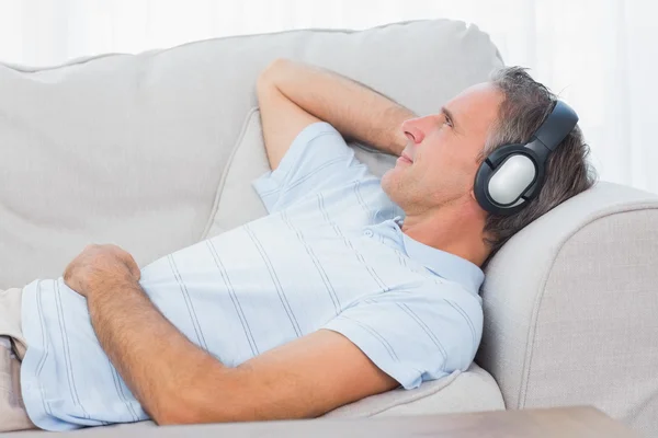 Человек лежит на диване и слушает музыку. — стоковое фото