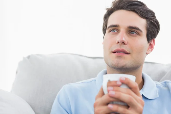Man holding a cup of coffee sat on the couch — Stock Photo, Image
