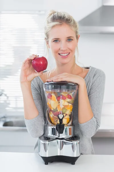 Mooie vrouw leunend op haar juicer vol met fruit en rood te houden — Stockfoto