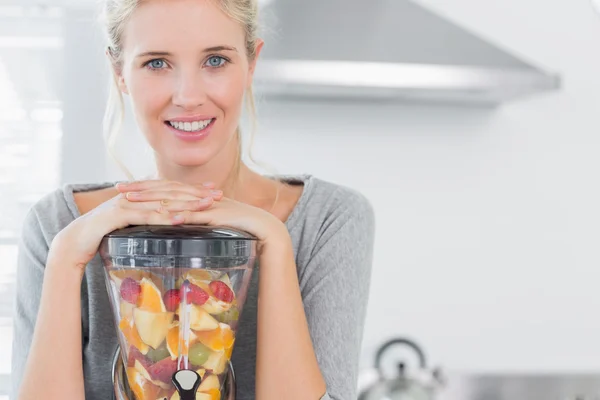 Mujer rubia apoyada en su exprimidor y sonriendo a la cámara — Foto de Stock