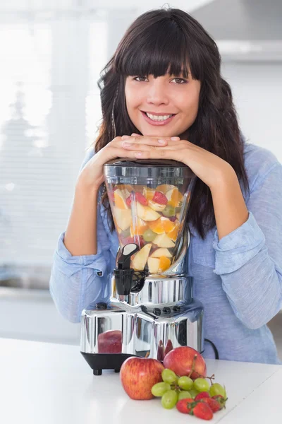 Lachende brunette leunend op haar juicer vol met fruit — Stockfoto