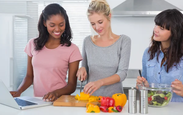 Cheerful friends making salad and using laptop for recipe — Stock Photo, Image