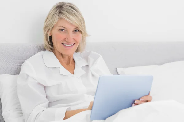 Mujer rubia sentada en la cama usando tableta pc — Foto de Stock