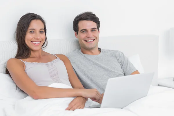 Retrato de um casal usando um laptop juntos deitados na cama — Fotografia de Stock